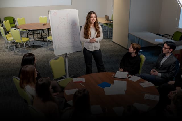 Sales & Development: Woman standing near whiteboard with charts, two people seated at table